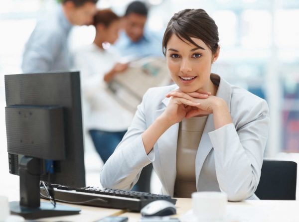 Pretty Caucasian business woman at office desk with colleagues in the back