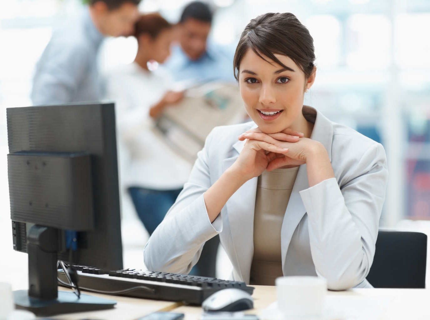 Pretty Caucasian business woman at office desk with colleagues in the back